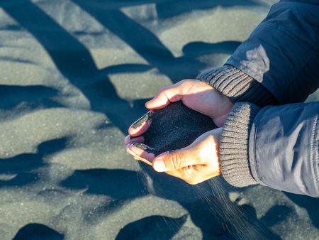 Black sand in two hands, amazing unique black sand beach landmark in Iceland in winter seasonの写真素材