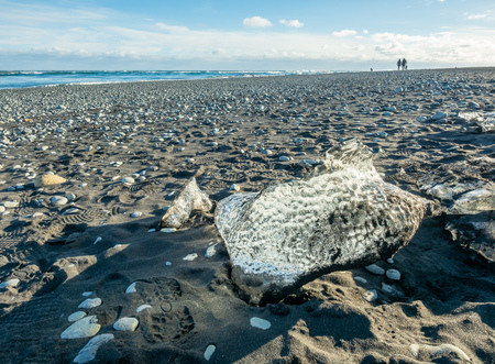 Ice pieces, glitter like diamonds, on black sand beach in winter season in Iceland, under cloudy blue skyの写真素材