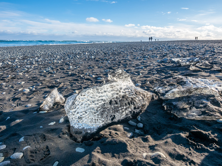 Ice pieces, glitter like diamonds, on black sand beach in winter season in Iceland, under cloudy blue skyの写真素材