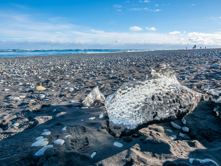 Ice pieces, glitter like diamonds, on black sand beach in winter season in Iceland, under cloudy blue skyの写真素材