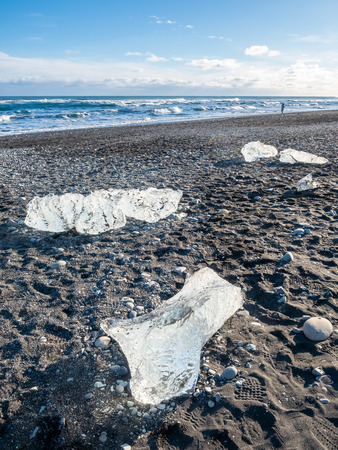 Ice pieces, glitter like diamonds, on black sand beach in winter season in Iceland, under cloudy blue skyの写真素材