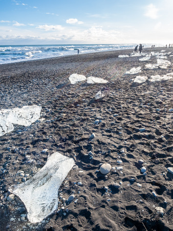 Ice pieces, glitter like diamonds, on black sand beach in winter season in Iceland, under cloudy blue skyの写真素材