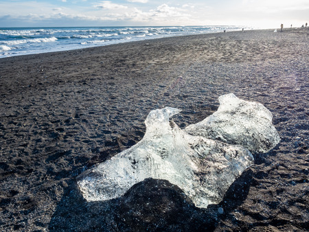 Ice pieces, glitter like diamonds, on black sand beach in winter season in Iceland, under cloudy blue skyの写真素材