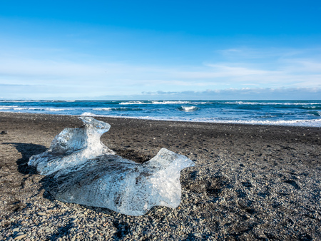 Ice pieces, glitter like diamonds, on black sand beach in winter season in Iceland, under cloudy blue skyの写真素材