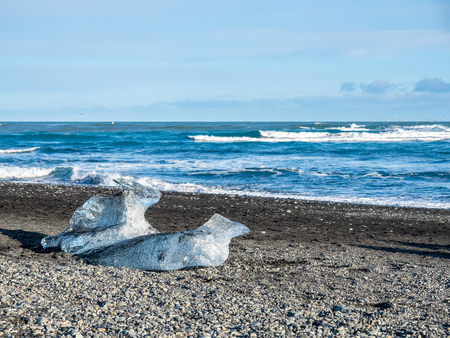 Ice pieces, glitter like diamonds, on black sand beach in winter season in Iceland, under cloudy blue skyの写真素材