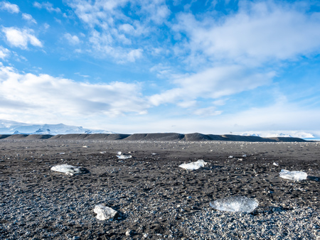 Ice pieces, glitter like diamonds, on black sand beach in winter season in Iceland, under cloudy blue skyの写真素材
