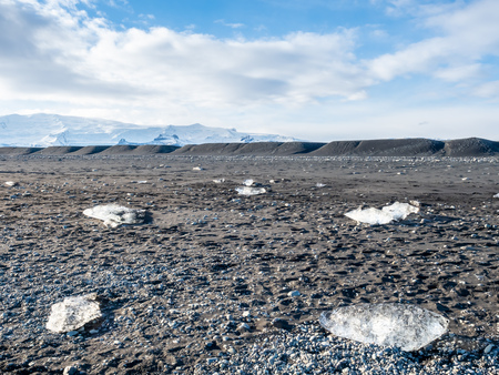 Ice pieces, glitter like diamonds, on black sand beach in winter season in Iceland, under cloudy blue skyの写真素材