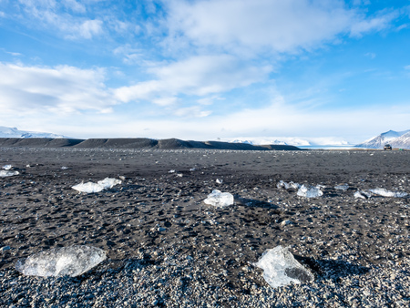 Ice pieces, glitter like diamonds, on black sand beach in winter season in Iceland, under cloudy blue skyの写真素材