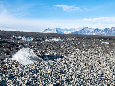 Ice pieces, glitter like diamonds, on black sand beach in winter season in Iceland, under cloudy blue skyの写真素材