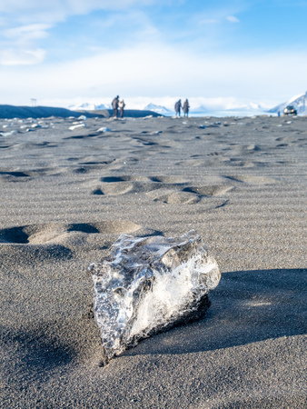 Ice pieces, glitter like diamonds, in heart shape on black sand beach in winter season in Iceland, under cloudy blue skyの写真素材
