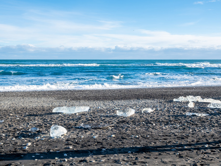 Ice pieces, glitter like diamonds, on black sand beach in winter season in Iceland, under cloudy blue skyの写真素材