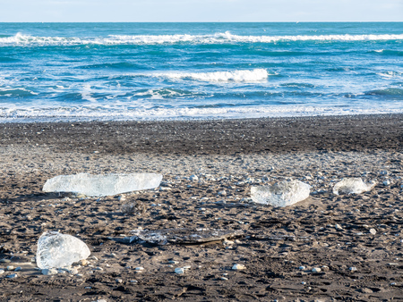 Ice pieces, glitter like diamonds, on black sand beach in winter season in Iceland, under cloudy blue skyの写真素材