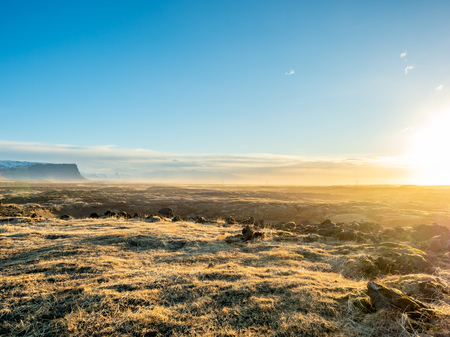 Natural scene with morning mist, field, mountains and cloudy blue sky in rural area in Icelandの写真素材