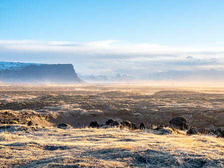 Natural scene with morning mist, field, mountains and cloudy blue sky in rural area in Icelandの写真素材