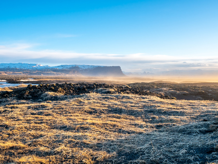 Natural scene with morning mist, field, mountains and cloudy blue sky in rural area in Icelandの写真素材