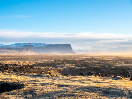 Natural scene with morning mist, field, mountains and cloudy blue sky in rural area in Icelandの写真素材