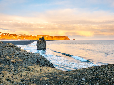 Arnardrangur, known as Eagle rock, at coastline near Dyrholaey arch surrounding with heavy wave and rocky mountains at south of Icelandの写真素材