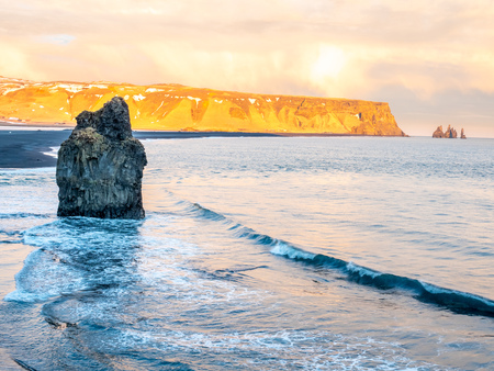 Arnardrangur, known as Eagle rock, at coastline near Dyrholaey arch surrounding with heavy wave and rocky mountains at south of Icelandの写真素材