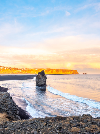 Arnardrangur, known as Eagle rock, at coastline near Dyrholaey arch surrounding with heavy wave and rocky mountains at south of Icelandの写真素材