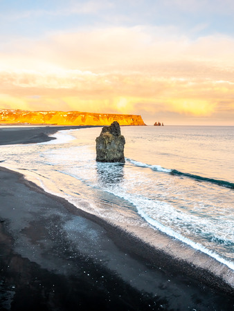Arnardrangur, known as Eagle rock, at coastline near Dyrholaey arch surrounding with heavy wave and rocky mountains at south of Icelandの写真素材