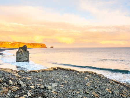 Arnardrangur, known as Eagle rock, at coastline near Dyrholaey arch surrounding with heavy wave and rocky mountains at south of Icelandの写真素材
