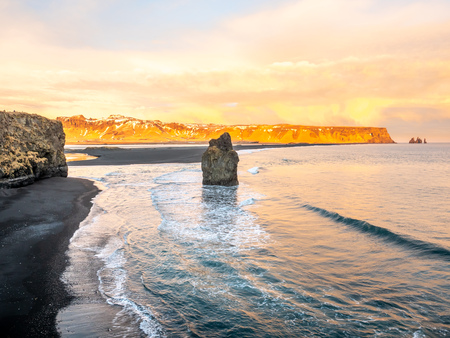 Arnardrangur, known as Eagle rock, at coastline near Dyrholaey arch surrounding with heavy wave and rocky mountains at south of Icelandの写真素材