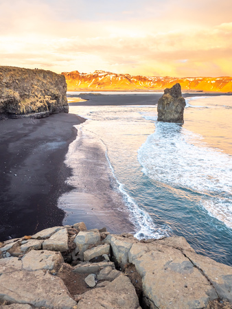 Arnardrangur, known as Eagle rock, at coastline near Dyrholaey arch surrounding with heavy wave and rocky mountains at south of Icelandの写真素材