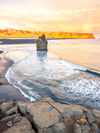 Arnardrangur, known as Eagle rock, at coastline near Dyrholaey arch surrounding with heavy wave and rocky mountains at south of Icelandの写真素材