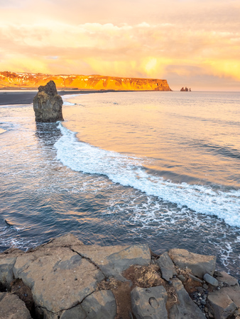 Arnardrangur, known as Eagle rock, at coastline near Dyrholaey arch surrounding with heavy wave and rocky mountains at south of Icelandの写真素材