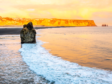 Arnardrangur, known as Eagle rock, at coastline near Dyrholaey arch surrounding with heavy wave and rocky mountains at south of Icelandの写真素材
