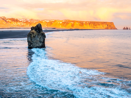 Arnardrangur, known as Eagle rock, at coastline near Dyrholaey arch surrounding with heavy wave and rocky mountains at south of Icelandの写真素材