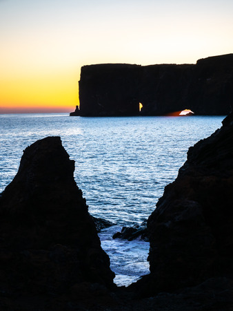 Silhouette view of Dyrholaey arch, mean 'the hill island with the door hole', amazing geology viewpoint near Vik town at south of Iceland, during twilight evening sky along coastlineの写真素材