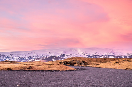 Snow cover mountains and lava rocks near Dyrholaey arch, landmark of Iceland, near Vik town, under twilight evening vanilla skyの写真素材