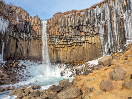Svartifoss waterfall, one of unique landmark in Iceland, located in Vatnajokull national park, like oasis in black larva sand plain, water freeze in winter seasonの写真素材
