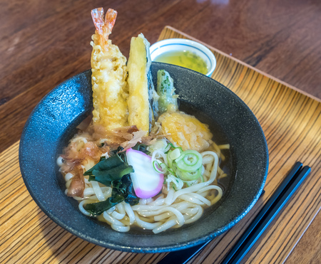 Japanese style noodle with fried crunchy shrimp, tempura, and seaweed in clear soup, black bowl in Japanの写真素材