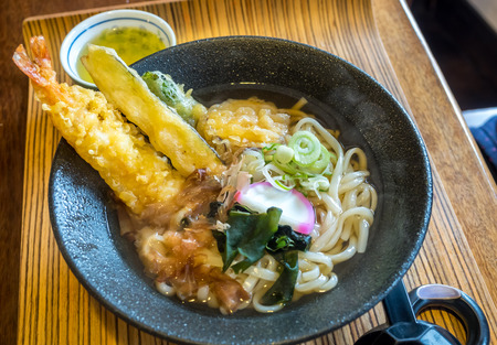 Japanese style noodle with fried crunchy shrimp, tempura, and seaweed in clear soup, black bowl in Japanの写真素材