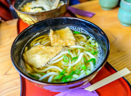 Udon, Japanese style noodle, with tofu in clear soup in black bowlの写真素材