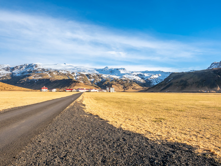 Rural road on drive trip under cloudy blue sky in Icelandの写真素材