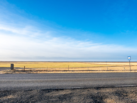 Rural road on drive trip under cloudy blue sky in Icelandの写真素材