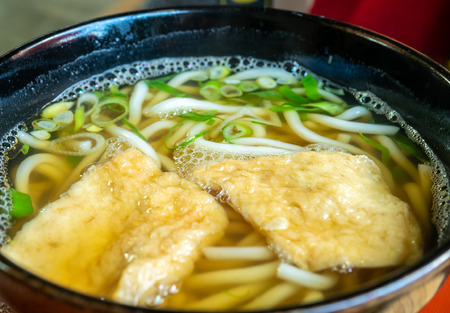 Udon, Japanese style noodle, with tofu in clear soup with spring onion in black bowlの写真素材
