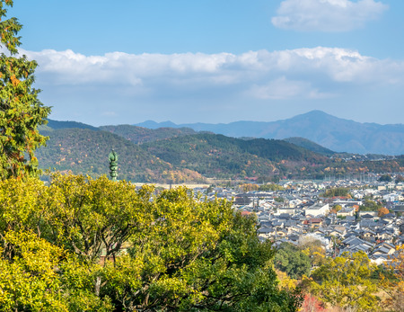 Arashiyama cityscape viewpoint with autumn tree forest under cloudy blue sky with mountains in background, Japanのeditorial素材