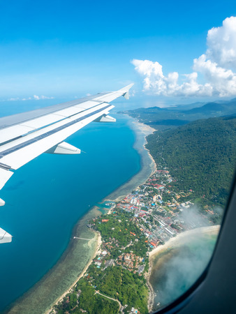 Island, sea, beach and cloudy blue sky view from aircraft window with its right wingの写真素材