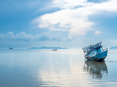 Fisherman boat aground over shallow sea water in evening under cloudy blue sky at island in Thailand