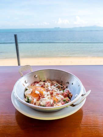Fried egg with sausage, ham and bacon on private pan with seascape view in summer season at Samui island, Thailandの写真素材