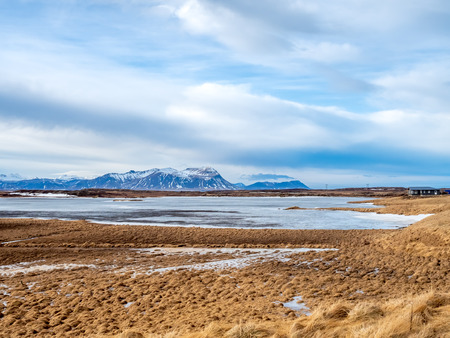Field with snow in winter season with moutains in background under cloudy blue sky in Icelandの写真素材