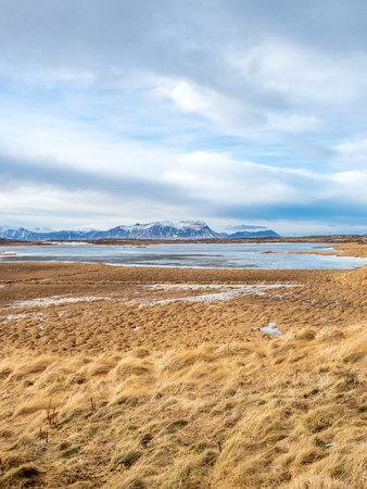 Field with snow in winter season with moutains in background under cloudy blue sky in Icelandの写真素材