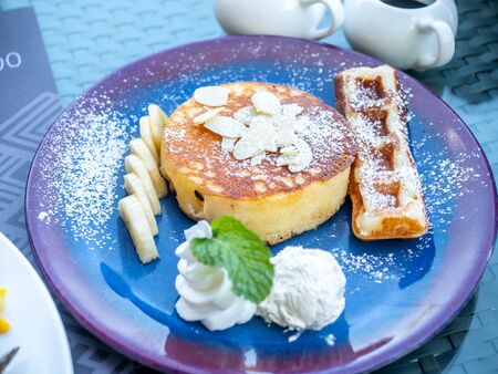 Fluffy pancake with a piece of waffle serve with banana, cream, syrup and honey on black dish for breakfastの写真素材
