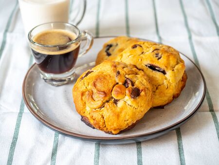 Chunky chewy chocolate chip soft cookie with cup of coffee and milk for breakfast, selective focus on melting chocolate chipsの写真素材
