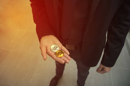 Hand holding a golden bitcoin, blurred background of legs and body. View from above, top-view. Concept of exchange value, money.の写真素材