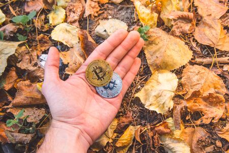 Hand holding a golden bitcoin, blurred background of legs and body. View from above, top-view. Concept of exchange value, money.の写真素材